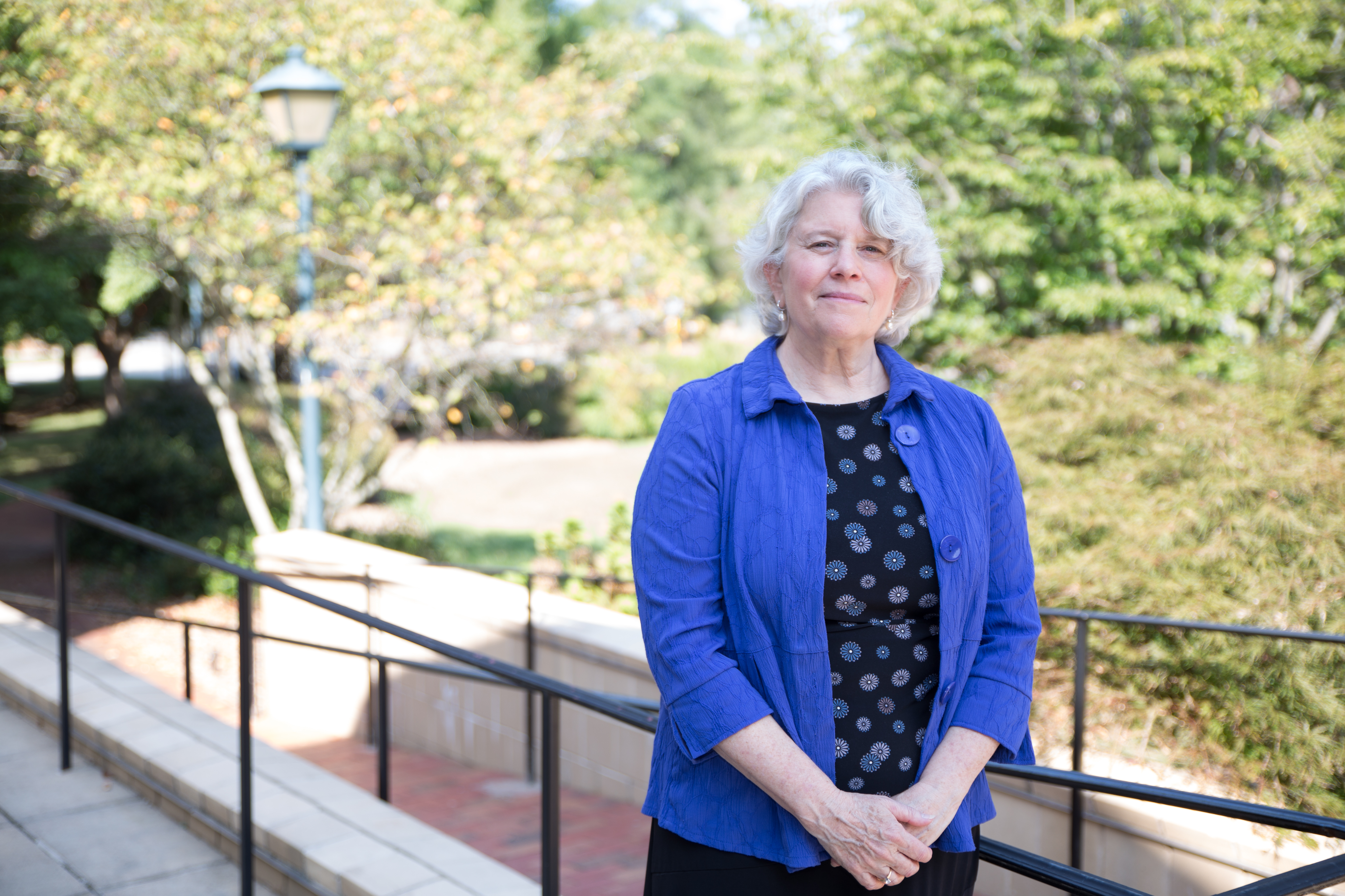 Frayda Bluestein stands in front of the School of Government in a blue jacket and black top.