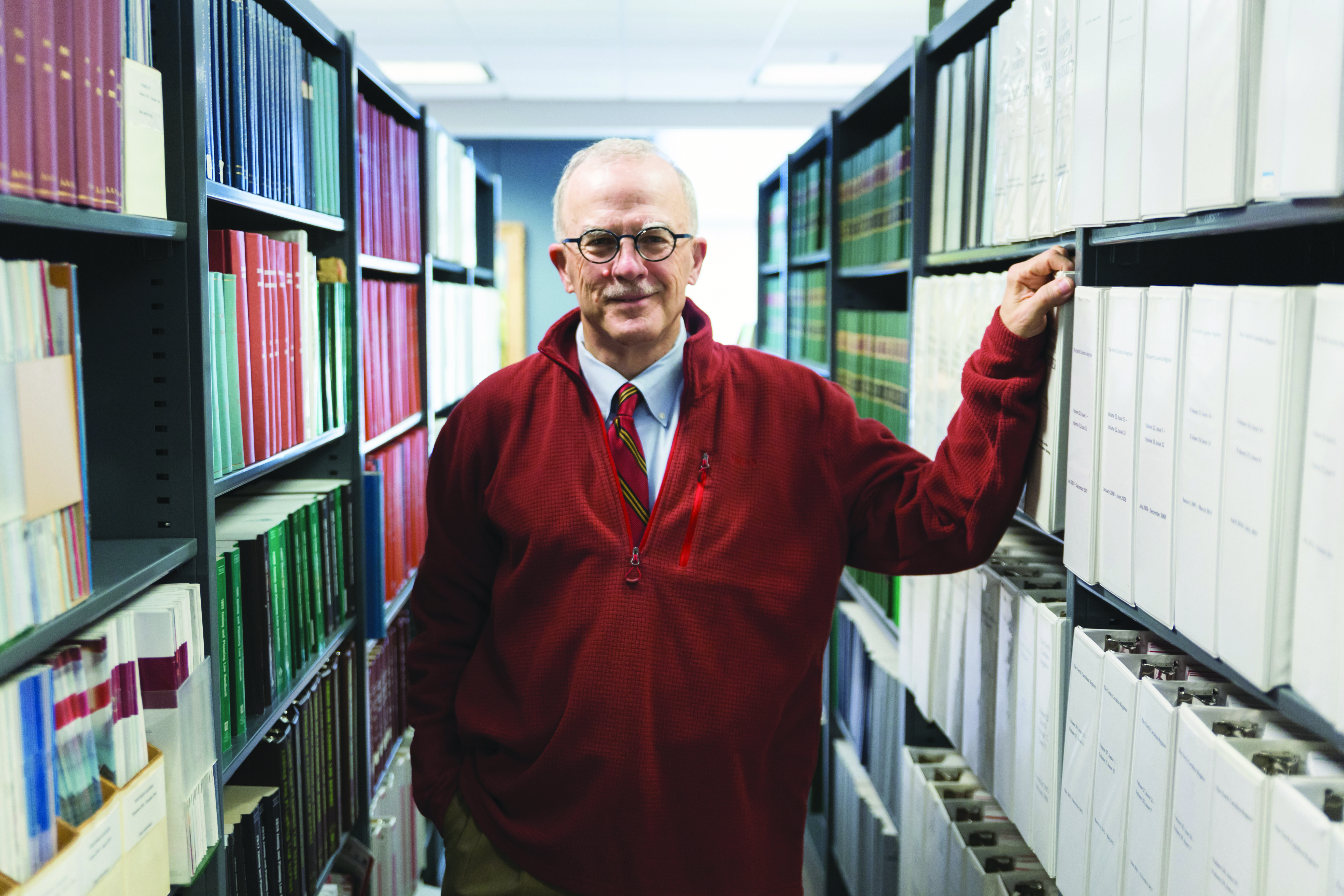 Dean Mike Smith stands in the Knapp Library, flanked on either side by bookshelves.