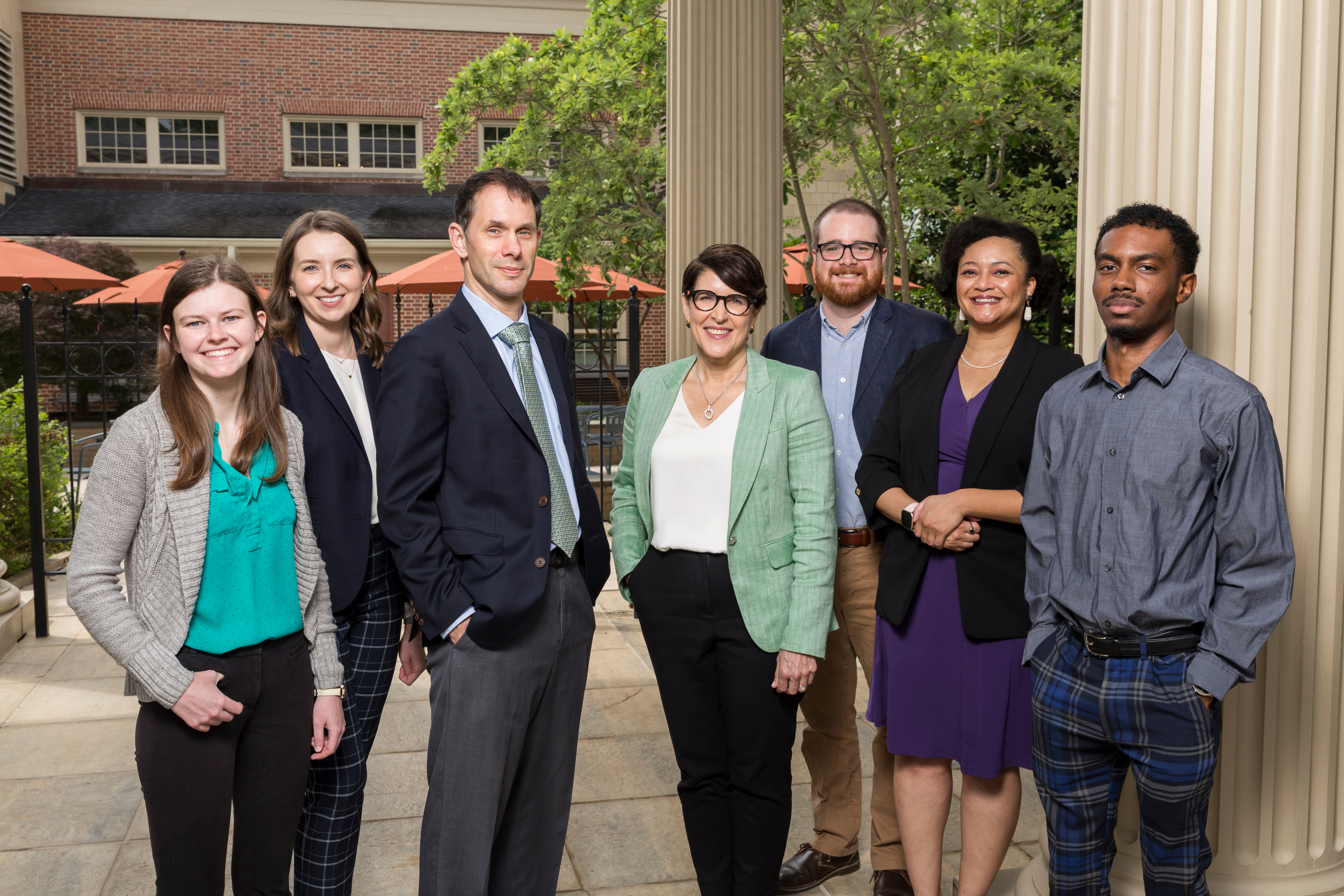 Seven people stand next to large columns in front of the School of Government building. They are wearing business clothes and smiling.