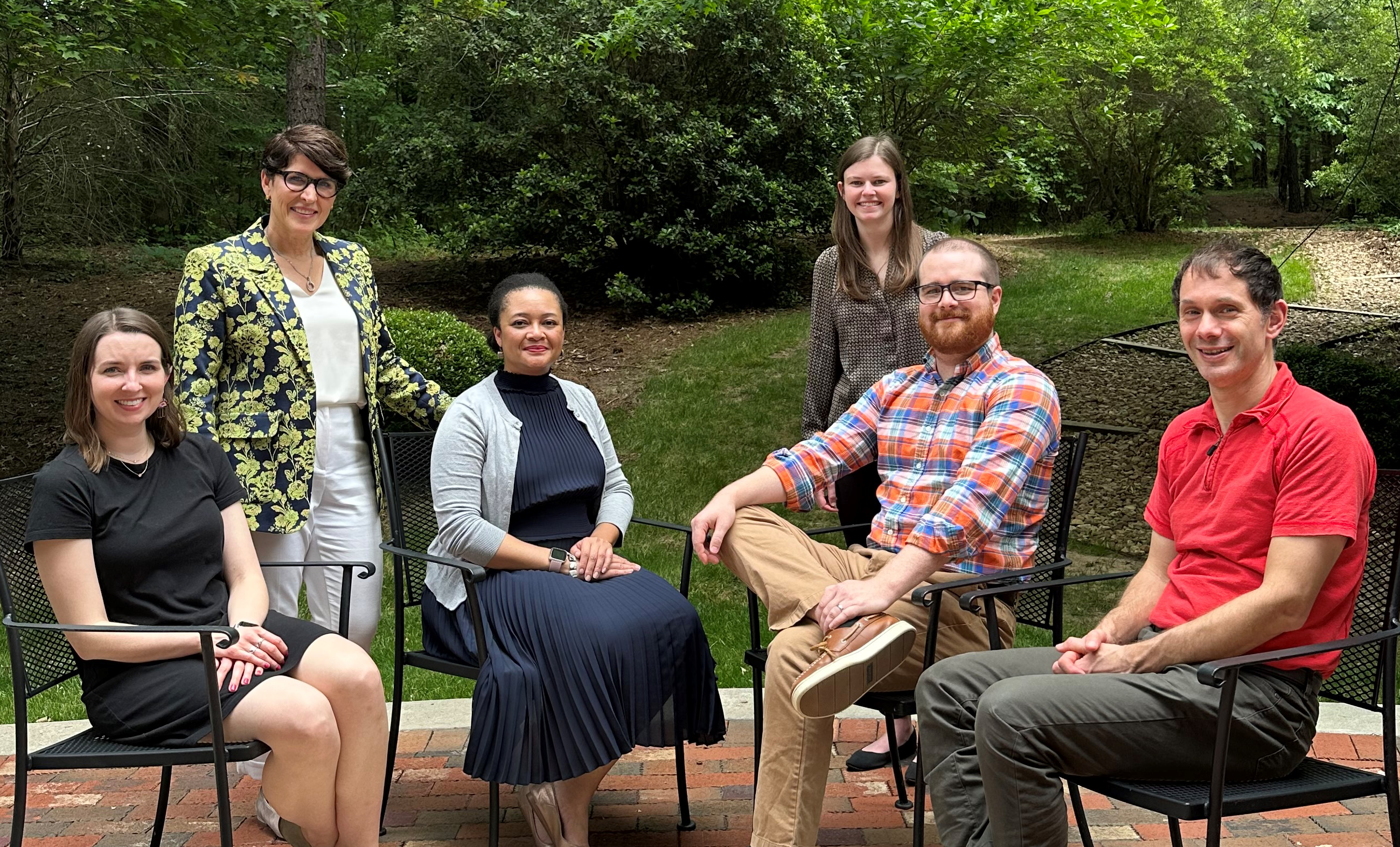 Six members of the Criminal Justice Innovation Lab team seated and standing in front of leafy trees and grass.