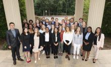 The group of cohort 5 fellows stands smilling between the pillars of the School of Government