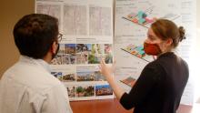 Two DFI staff members in masks talk to each other while standing in front of a map.