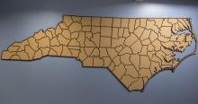 A mounted corkboard map in the shape of North Carolina hangs on a blue wall